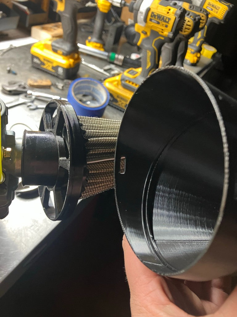 Hand holding 3D printed rain hood cup next to stock air filter showing fitment on Briggs engine