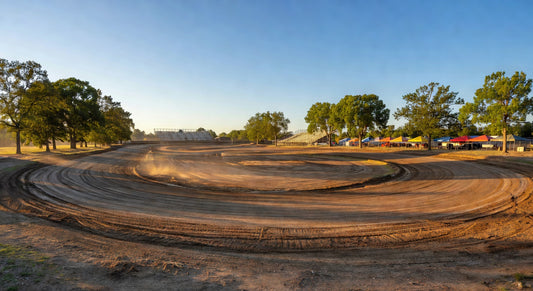 Wide scenic landscape of a dirt oval kart track on a sunny day