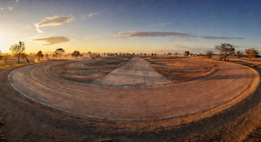 Dirt oval kart track at sunset with expansive pit area.