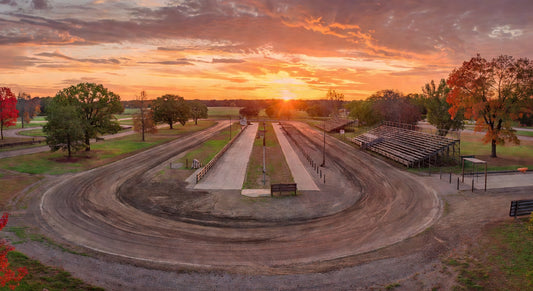 Sunset view over a quiet dirt oval kart track, pits ready for action.
