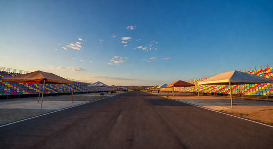 Paved sprint kart track at golden hour with grandstands and open pits.