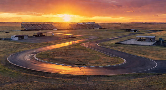 Paved sprint kart track at sunset with open fields and grandstands