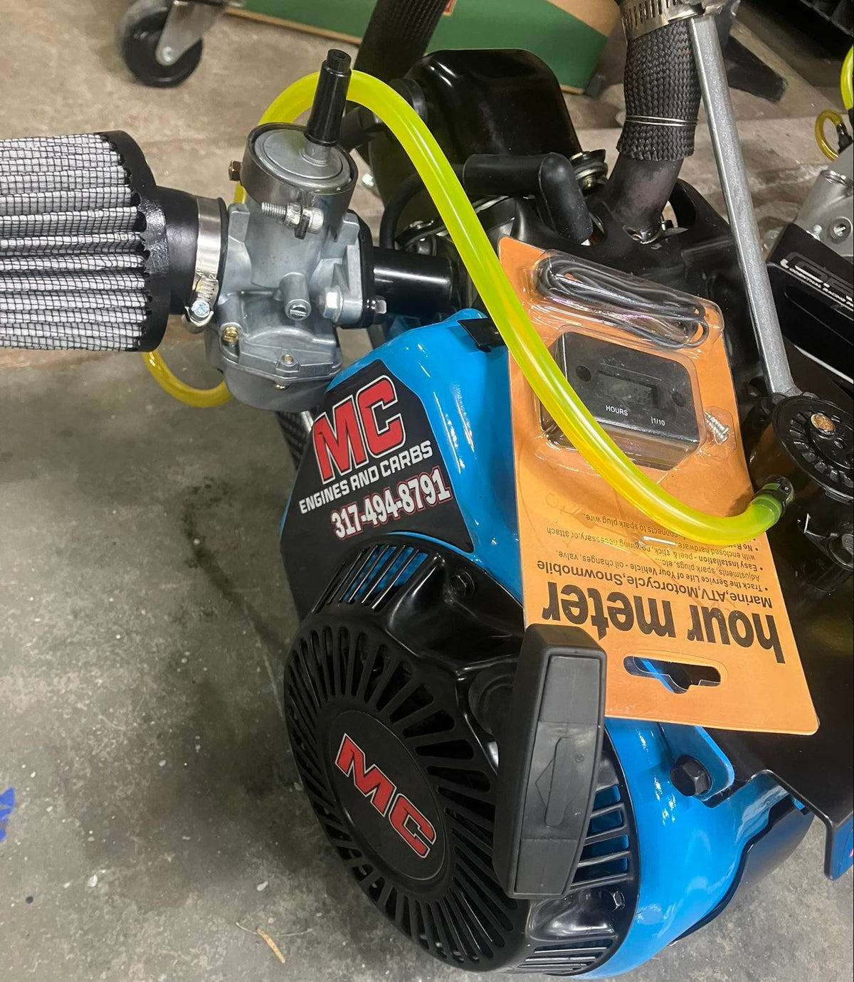 Blue colored case on a LO206 engine sitting on  small peice of wood not visible, that is also sitting on concrete. Engine has the fuel filter, exhaust, and fuel pump visible. Located in a shop.