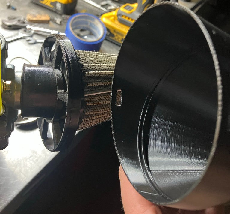 Hand holding 3D printed rain hood cup next to stock air filter showing fitment on Briggs engine