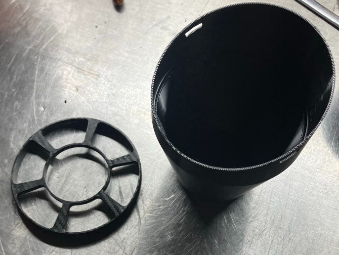 Two-piece black PETG rain hood base and cup on metal workbench next to pliers and wrenches