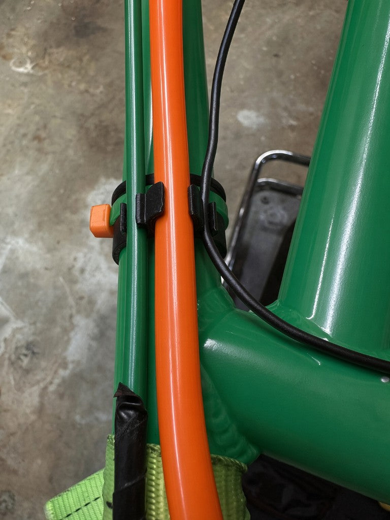 Black 3D printed fuel line cable management clip installed on green kart chassis holding orange 3/8 inch fuel line and black cable with zip ties on a concrete surface
