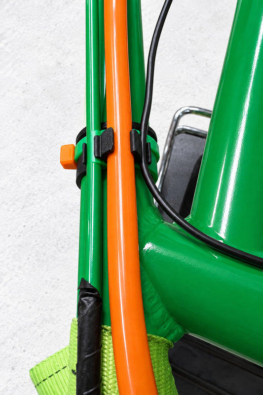 Black 3D printed fuel line cable management clip installed on green kart chassis holding orange 3/8 inch fuel line and black cable with zip ties on a concrete surface