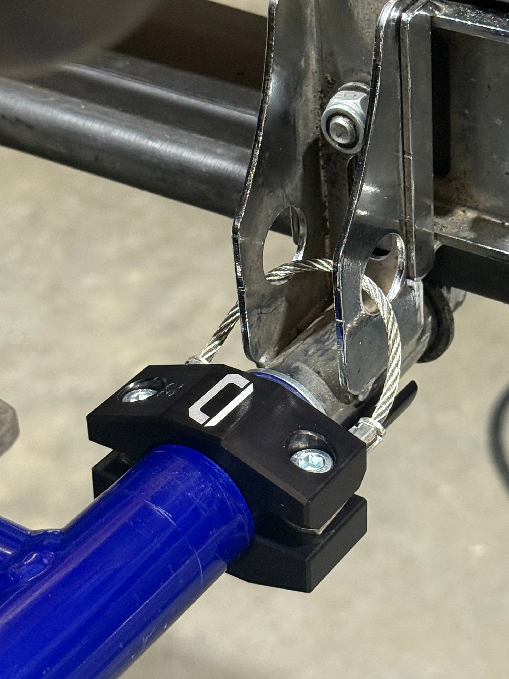 EZBR rear bumper safety clamp installed on blue kart bumper tube secured to chassis bracket with cable routed on concrete background