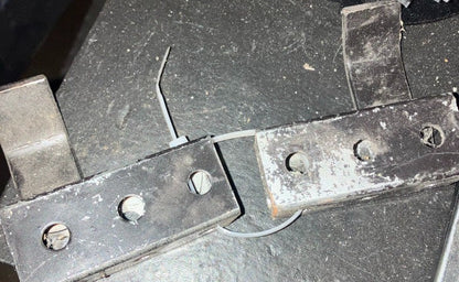 Bare metal steel kart stand pickup bracket showing rectangular body, mounting holes and wire retaining clip on a workbench