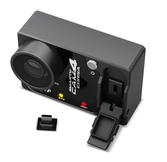 Top view of a sport cam corsa 4 camera, with a white background and the memory door open showing two lights a yellow and red led. A charger sitting on side.