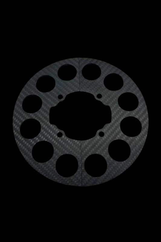 Woven carbon fiber split sprocket guard shown against black background, circular disc with precision lightening holes and central cutout for the mini hub.