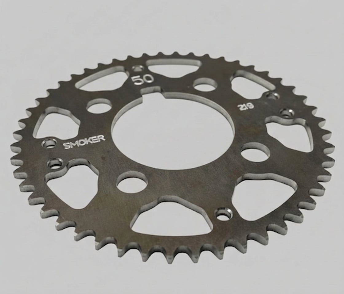 Overhead product shot of the silver Smoker Performance ultra-light one-piece #219 sprocket on a black background, clearly showing the tooth profile, lightening holes, stamped SMOKER logo, and example 50T marking.