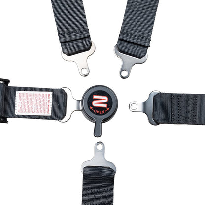 Close-up of Zamp 5 point youth harness camlock buckle with all five metal latch tongues detached showing individual attachment points and warning label on a white background